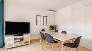 A modern dining area with a TV, a dining table, chairs, and a potted plant. - Aux Arènes, 30m from Les Arènes, Balcony, AC (Nîmes)