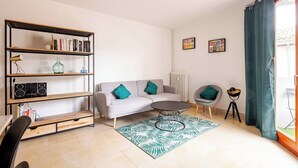 A modern living room with a grey sofa, a wooden bookshelf, a round coffee table, and a patterned rug. - Aux Arènes, 30m from Les Arènes, Balcony, AC (Nîmes)