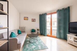 A modern living room with a sofa, a coffee table, a TV, and a balcony with curtains. - Aux Arènes, 30m from Les Arènes, Balcony, AC (Nîmes)