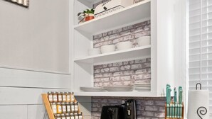 Eine Küche mit grauen Schränken, einer Holz Arbeitsplatte und einer Ziegelrückwand. Auf der Arbeitsplatte befinden sich eine Kaffeemaschine, ein Gewürzregal und ein Messerblock.