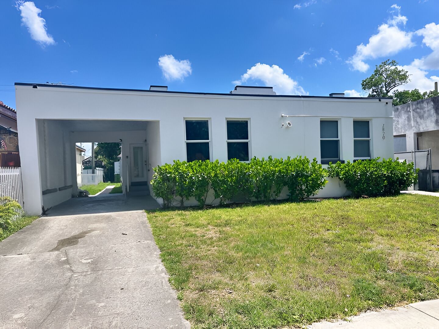 A modern two-story building with a flat roof, a covered entrance, and a small front yard with green shrubs.