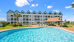 Un hotel con una piscina grande, varios balcones y un césped bien cuidado.