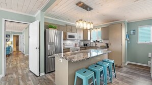 Una cocina moderna con una isla central, electrodomésticos de acero inoxidable y taburetes de bar color turquesa.