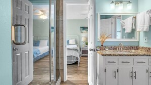 Habitación de hotel con cama, baño con lavabo y espejo, y una puerta que da a otra habitación.