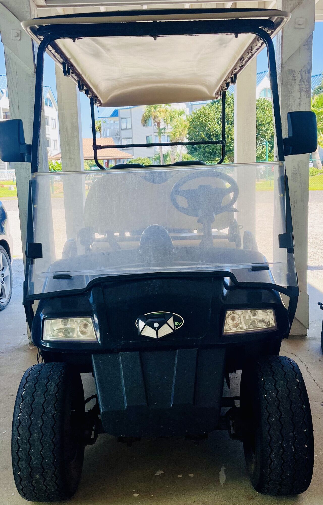 A golf cart parked under a covered area with a clear view of the surrounding buildings and greenery.