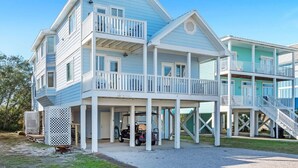 Een tweelaags huis aan het strand met een balkon, een overdekte veranda en een garage.