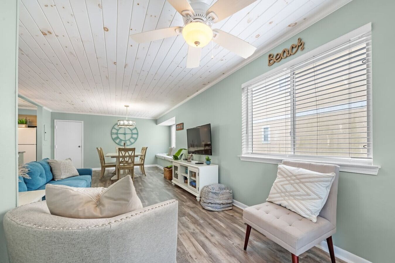 A living room with a ceiling fan, a TV, a dining area, and a window with blinds.