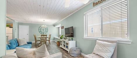 A living room with a ceiling fan, a TV, a dining area, and a window with blinds.