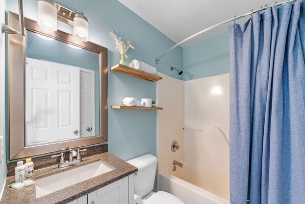 A bathroom with a sink, toilet, shower, and a mirror with lights.