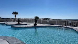 A clear swimming pool with a wooden deck, palm trees, and a fence. - Luxury 6-Bedroom Beachside Oasis | Resort Living with 7 Pools & 3 Jacuzzis! (Gulf Shores)
