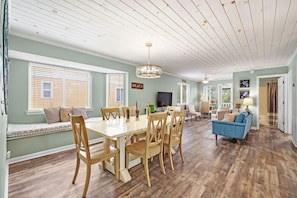 A spacious living area with a dining table, wooden chairs, a blue sofa, and a ceiling with exposed beams.