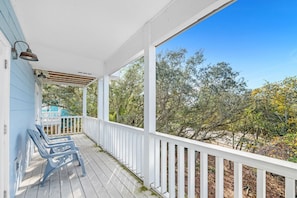 A covered porch with white railings, a blue bench, and a view of trees and a building in the background.