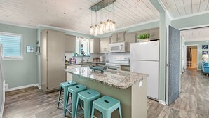 A modern kitchen with a central island, bar stools, a microwave, stove, and a refrigerator. - Luxury 6-Bedroom Beachside Oasis | Resort Living with 7 Pools & 3 Jacuzzis! (Gulf Shores)