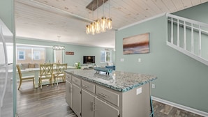 A modern kitchen with a granite countertop, wooden cabinets, and a dining area with a bench and chairs. - Luxury 6-Bedroom Beachside Oasis | Resort Living with 7 Pools & 3 Jacuzzis! (Gulf Shores)