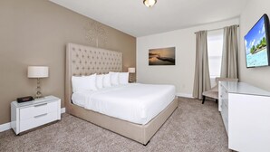 A hotel room with a large bed, a bedside table, a desk, a chair, a TV, and a painting on the wall.