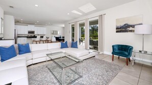 A modern living room with a white sectional sofa, a glass coffee table, and a teal armchair.