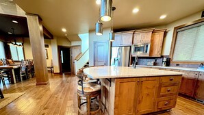 A spacious kitchen with wooden cabinets, a large island with stools, stainless steel appliances, and a visible staircase leading to another level. - 3 Bedroom w/ Game Room / Gourmet Kitchen / Community Pool - MNT VIEW IS AMAZING! (Cle Elum)