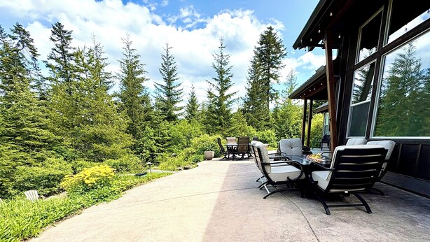 An outdoor patio with a dining table and chairs, surrounded by lush greenery and tall trees. - 3 Bedroom w/ Game Room / Gourmet Kitchen / Community Pool - MNT VIEW IS AMAZING! (Cle Elum)