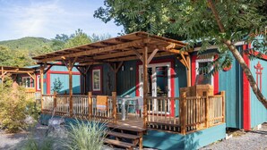 Un chalet rustique doté d’une terrasse en bois, d’un patio couvert et d’un petit espace extérieur aménagé pour s’asseoir.