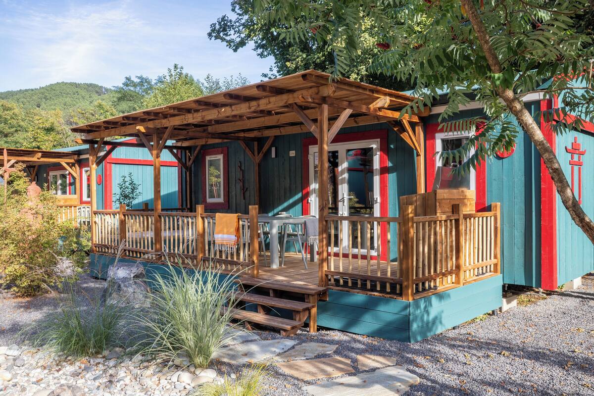 A rustic cabin with a wooden deck, a covered patio, and a small outdoor seating area.