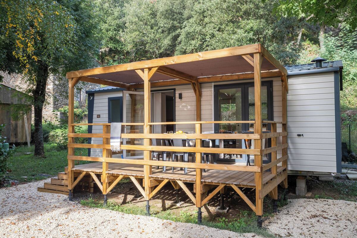 A wooden decked structure with a covered seating area, adjacent to a building with a sliding door.
