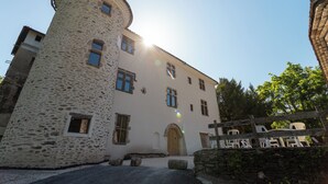 Une tour de pierre adossée à un bâtiment blanc, doté de nombreuses fenêtres et d’une porte en bois.