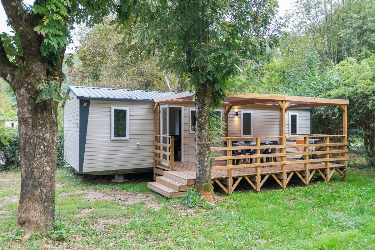 A small cabin with a wooden deck and a covered porch, surrounded by trees.