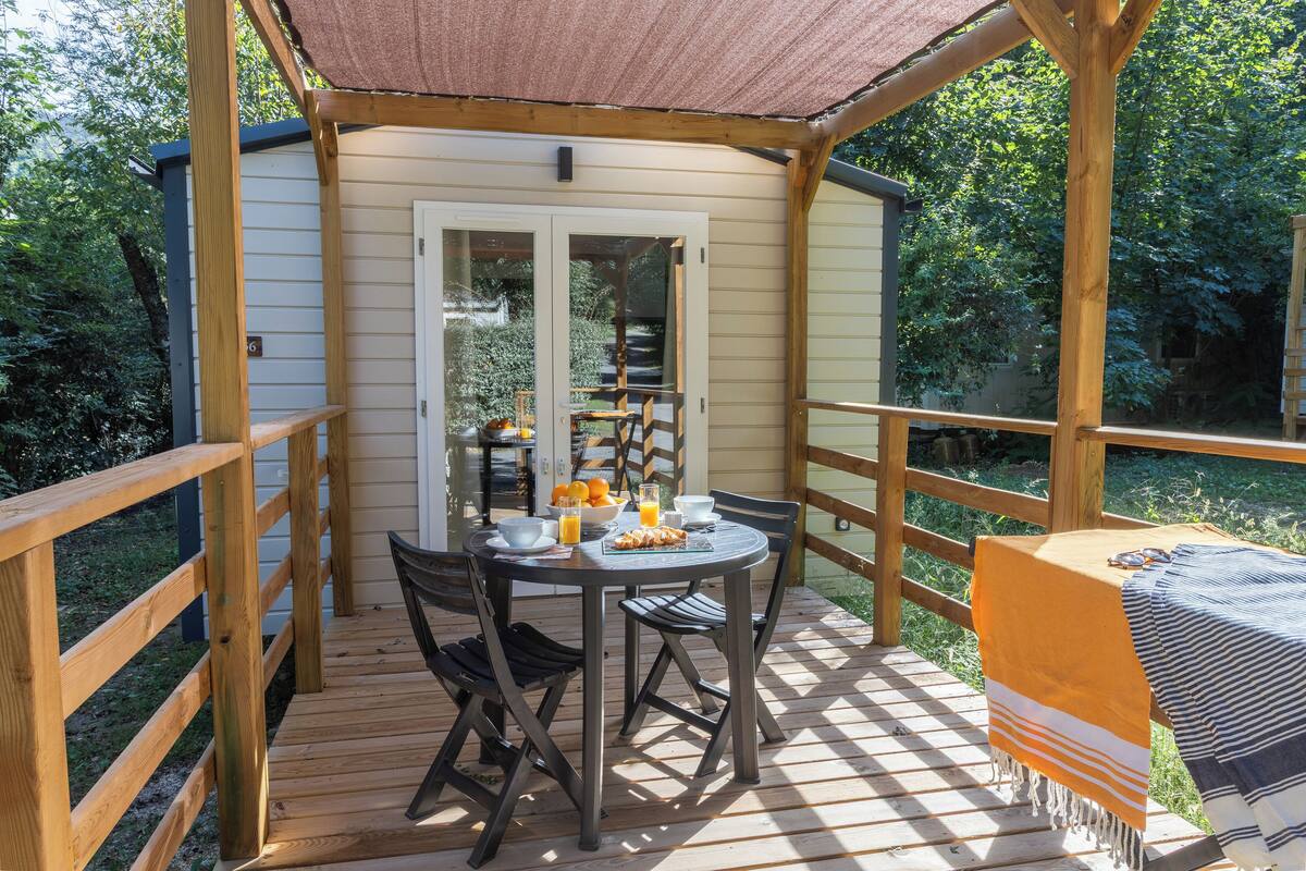 A wooden deck with a table set for breakfast, including bowls, oranges, and a bottle of orange juice.