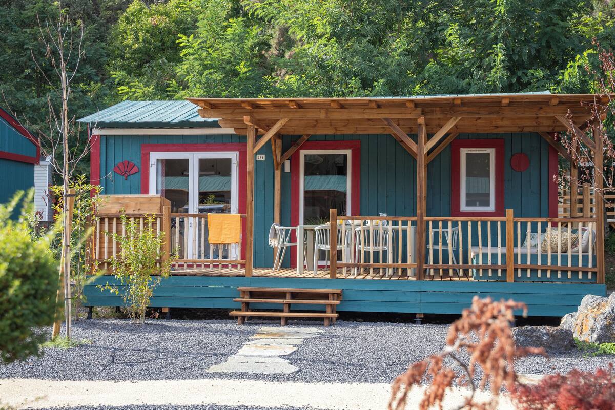 A small cabin with a wooden deck, a covered porch, and a small outdoor seating area.