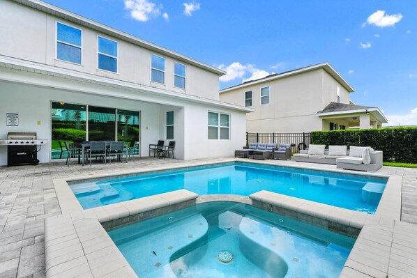 A swimming pool with a sunken area, outdoor seating, and a barbecue grill.