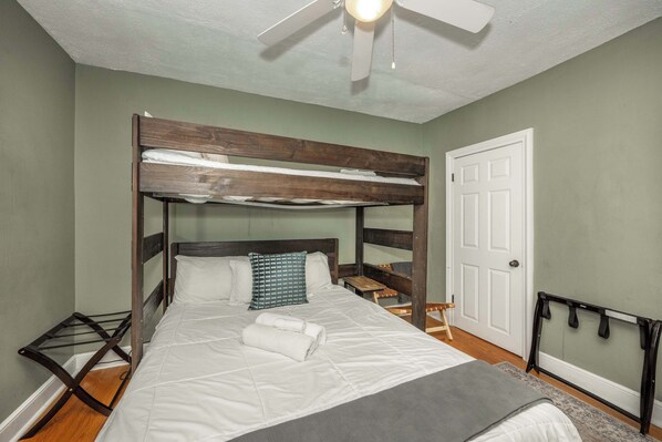 A bunk bed with a wooden headboard, a white mattress, and a grey blanket. There is a ceiling fan, a white door, and a small wooden bench. - La Dolce Vita Retreat w Hot Tub (Columbus)