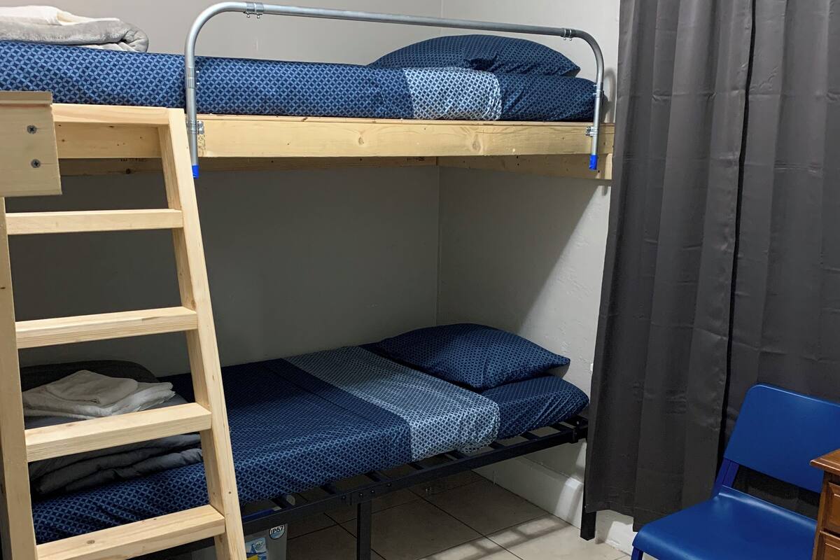 Dormitorio con literas, una escalera de madera, una silla azul y un pequeño armario de madera.