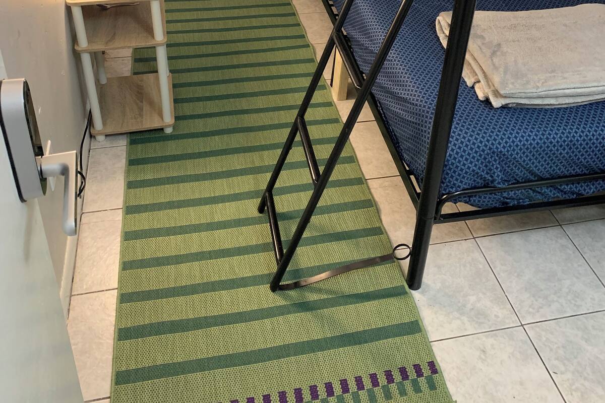 Habitación con literas, una alfombra verde a rayas, una mesita de noche con lámpara y una colcha azul estampada.