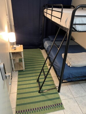 A bunk bed room with a green striped rug, a bedside table with a lamp, and a blue patterned bedspread. - Lenny's Southy Hostel (St. Petersburg)