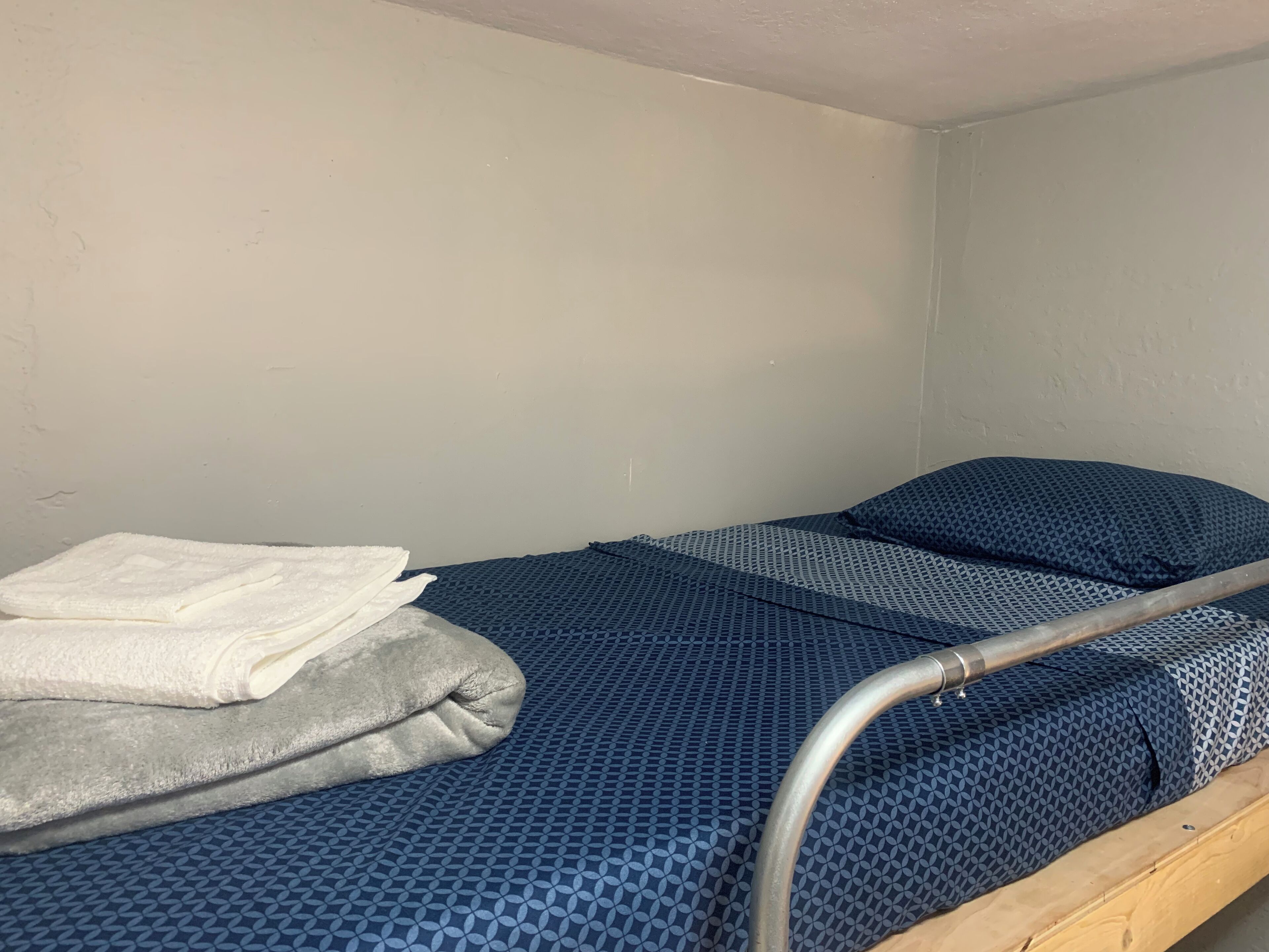 Ein Einzelbett mit Metallgestell, einer blauen, gemusterten Matratze und einem weißen, darübergelegten Handtuch.