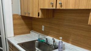 A kitchen with wooden cabinets, a stainless steel sink, and a marble countertop. - Lenny's Southy Hostel (St. Petersburg)