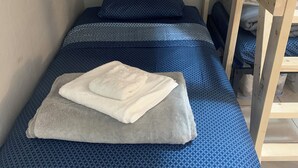 A small, single-bed room with a wooden headboard and a metal frame. The bed has a blue patterned bedspread and two pillows. A folded white towel is placed on the bed. - Lenny's Southy Hostel (St. Petersburg)