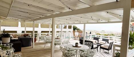 Une terrasse extérieure avec des chaises et des tables en métal blanc, un plancher en bois et une clôture blanche.