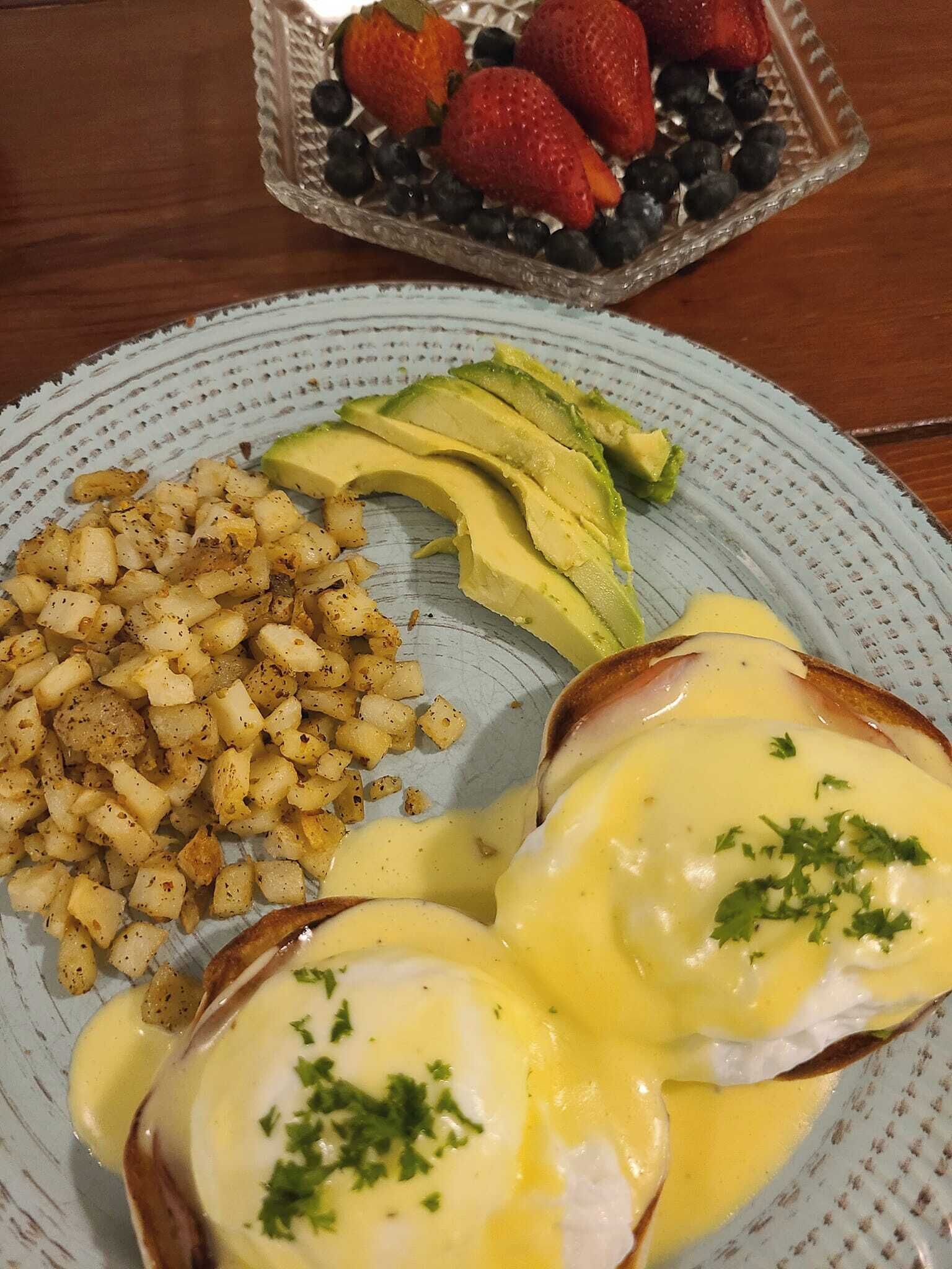 A plate with eggs benedict, avocado slices, and seasoned potatoes.