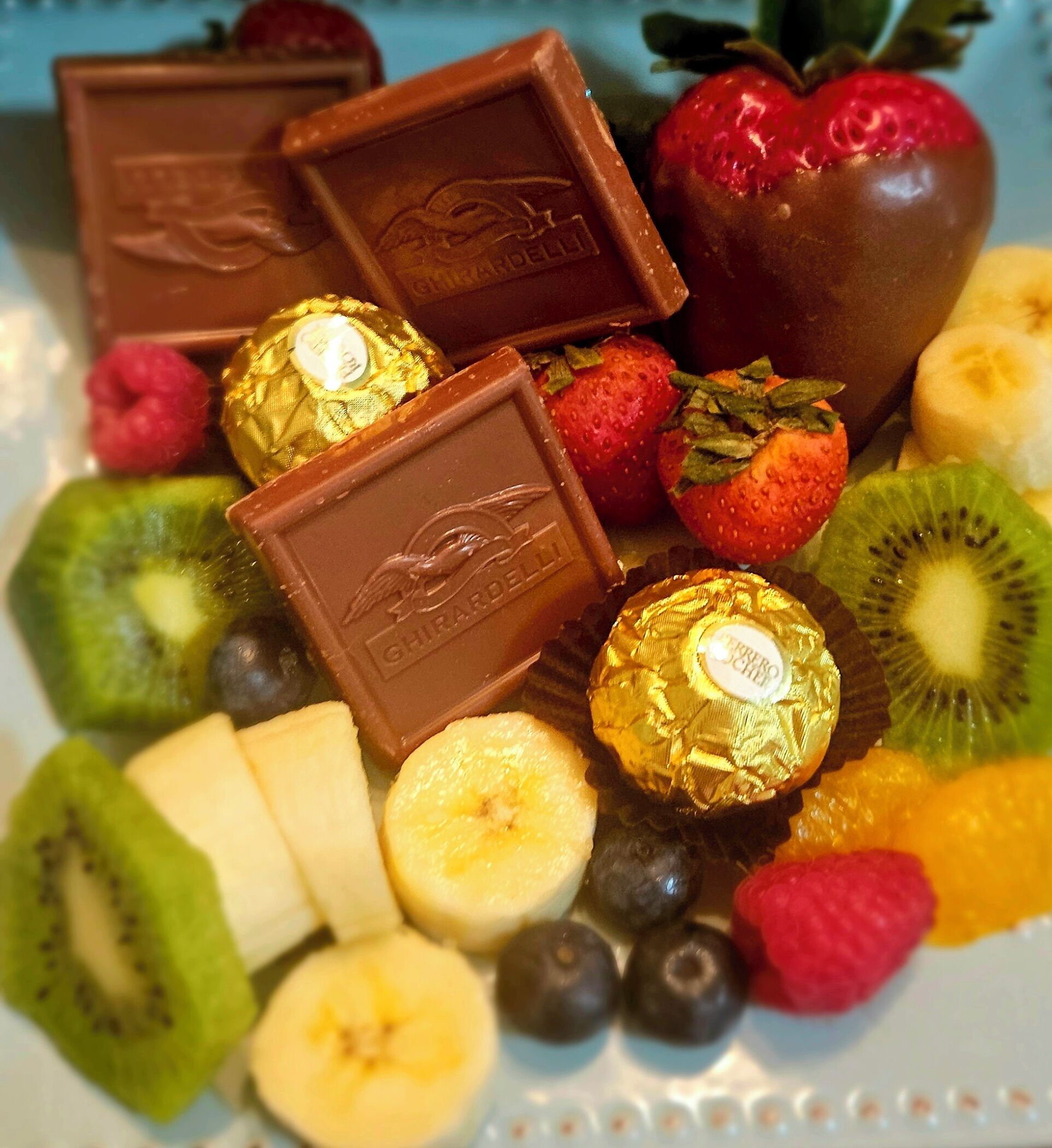 A plate with assorted chocolates, strawberries, kiwi, bananas, and blueberries.
