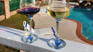 Dos copas de vino en un balcón con vistas a una piscina y al océano.