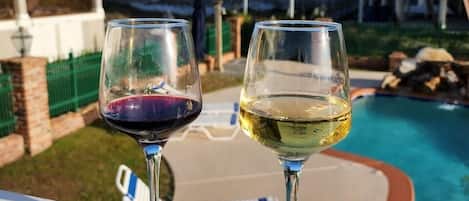 Two wine glasses on a balcony overlooking a pool and ocean view.
