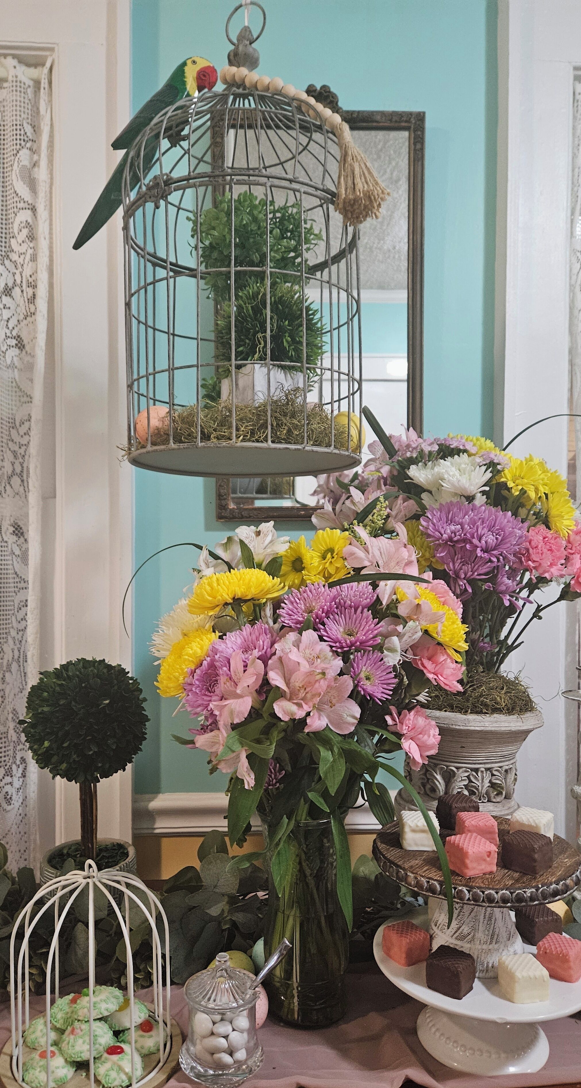 Una habitación con una jaula de pájaros, un florero con flores y un pastelero con varios dulces.