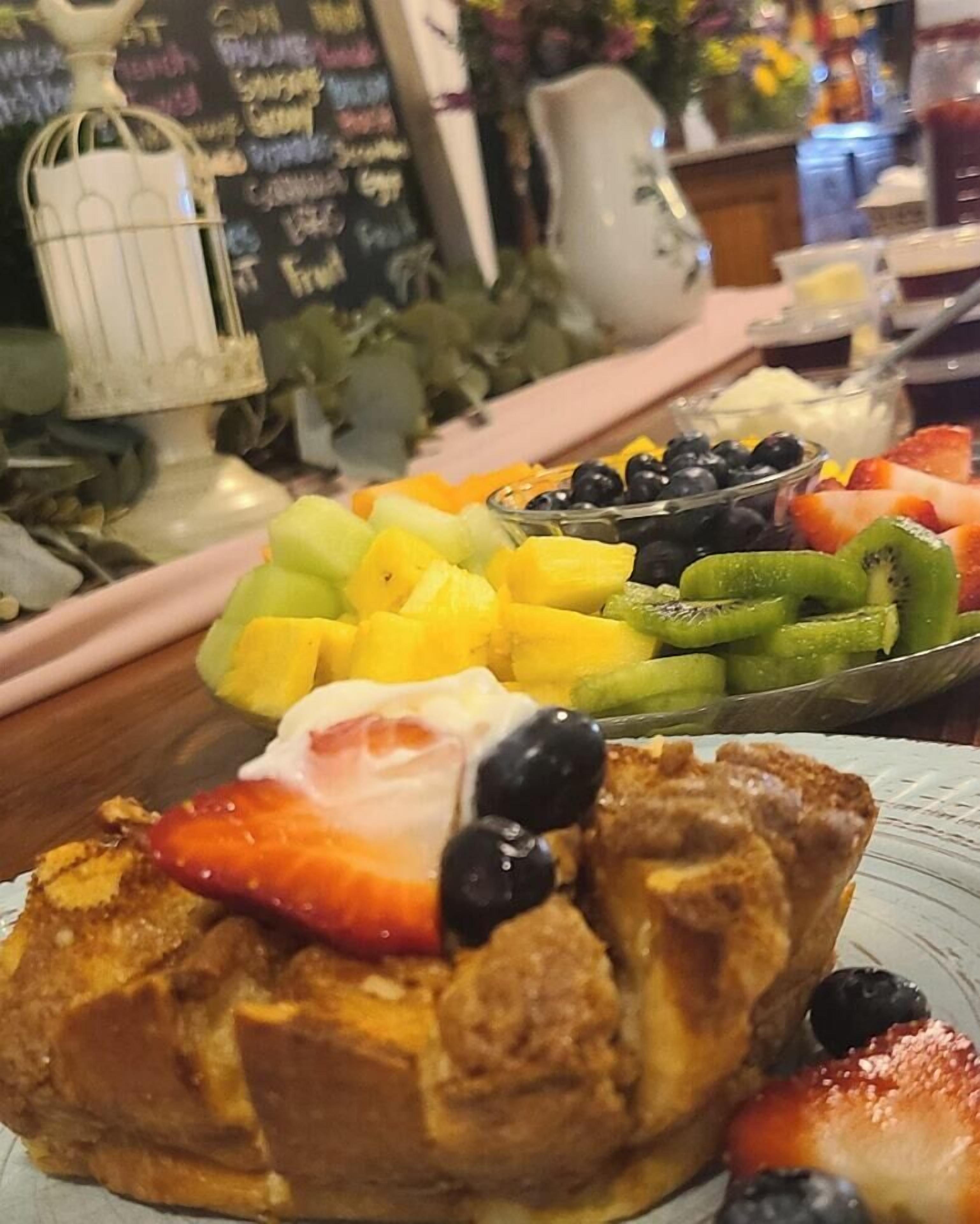 A breakfast buffet with various fruits and a breaded item topped with strawberries and blueberries.