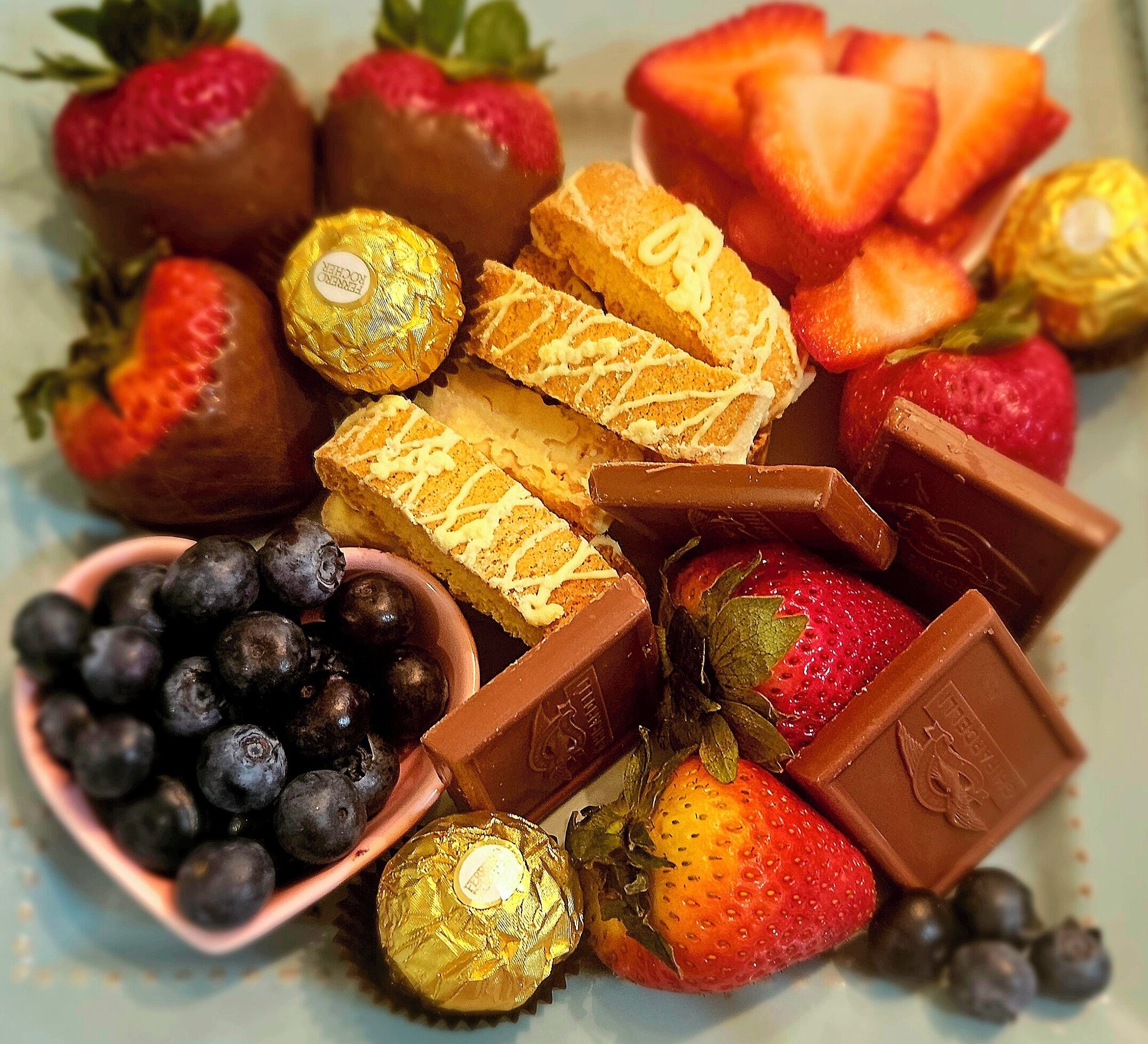 A variety of chocolates, strawberries, and blueberries arranged on a plate.