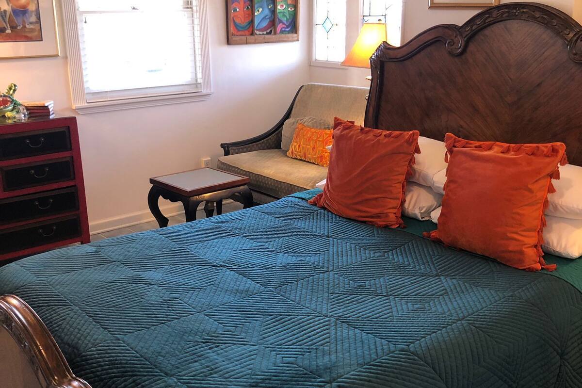 A bedroom with a large bed, a wooden headboard, a nightstand, a dresser, and a window with blinds.