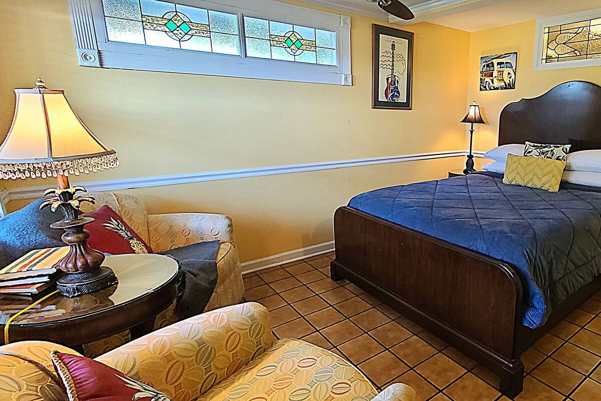 A bedroom with a bed, two bedside tables, a chair, a lamp, and a window with stained glass.