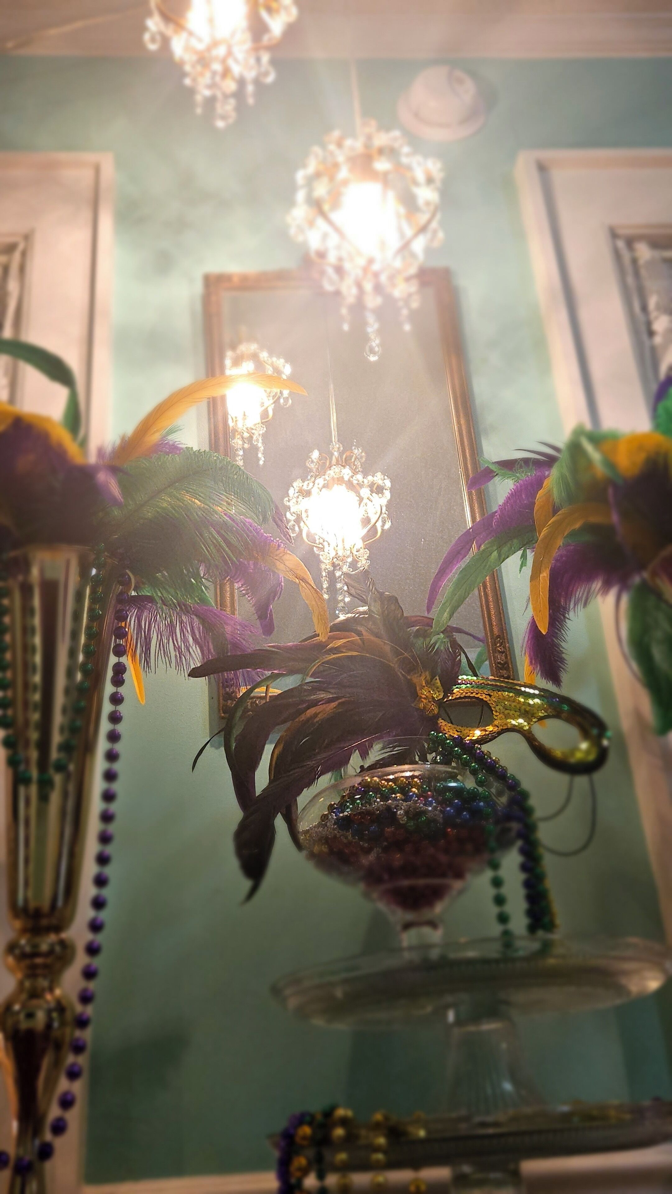 A room with a chandelier, a mirror, and decorative items including a vase with beads and feathers.