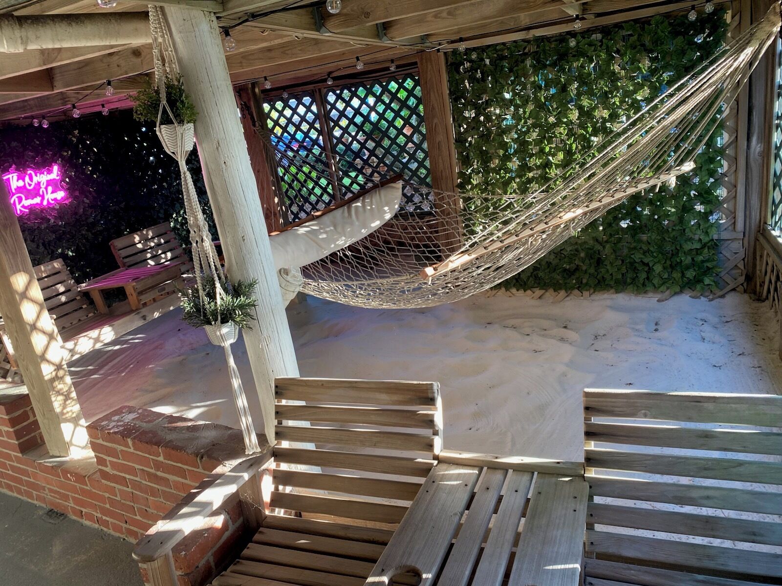 Un banco de madera y una hamaca bajo una pérgola de madera con un letrero de neón.