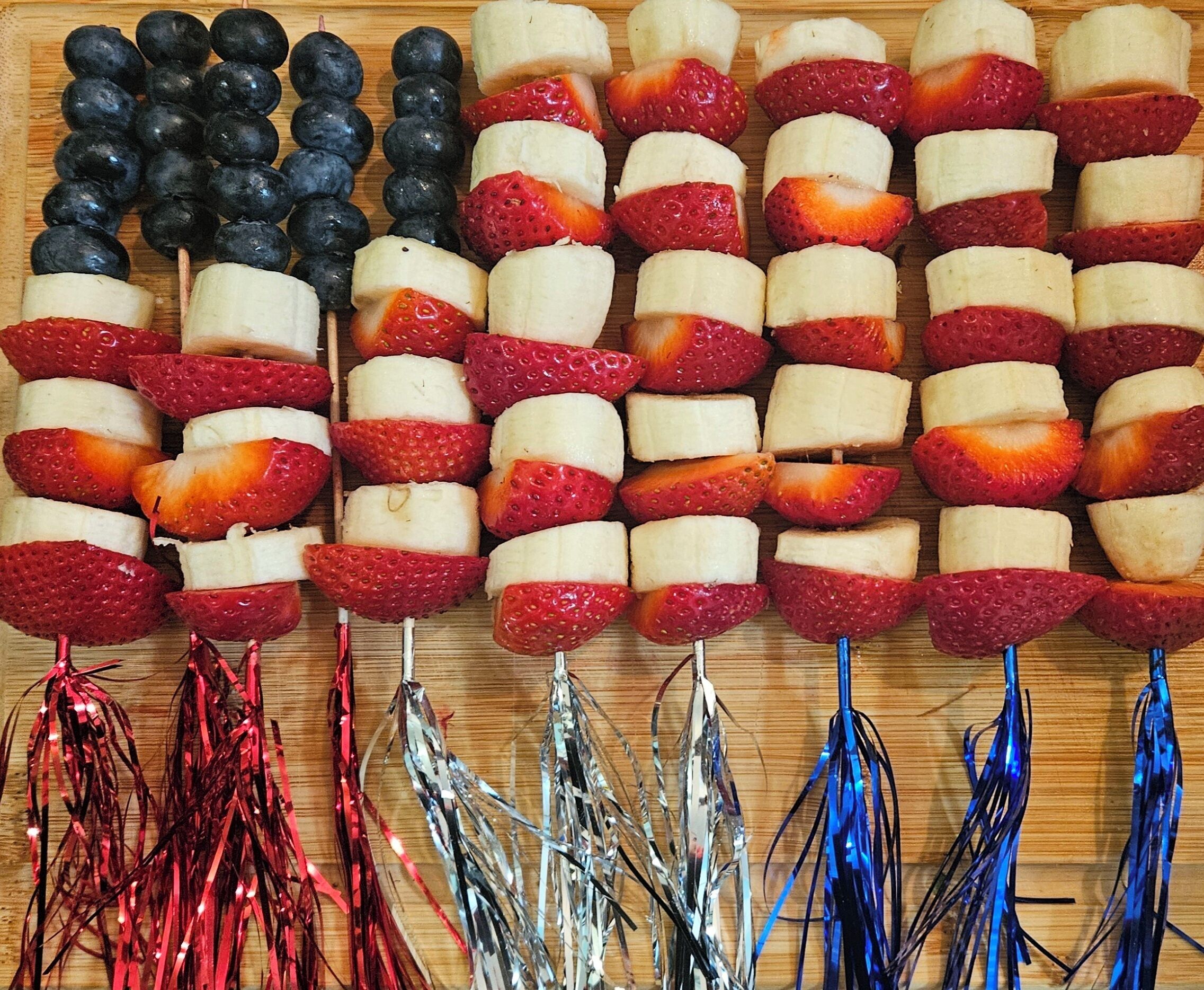 A wooden board with fruit skewers arranged in rows.